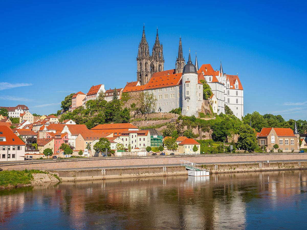 Historische Stadt Meissen mit Albrechtsburg, Meissner Dom und bunten Häusern am Elbufer unter blauem Himmel.