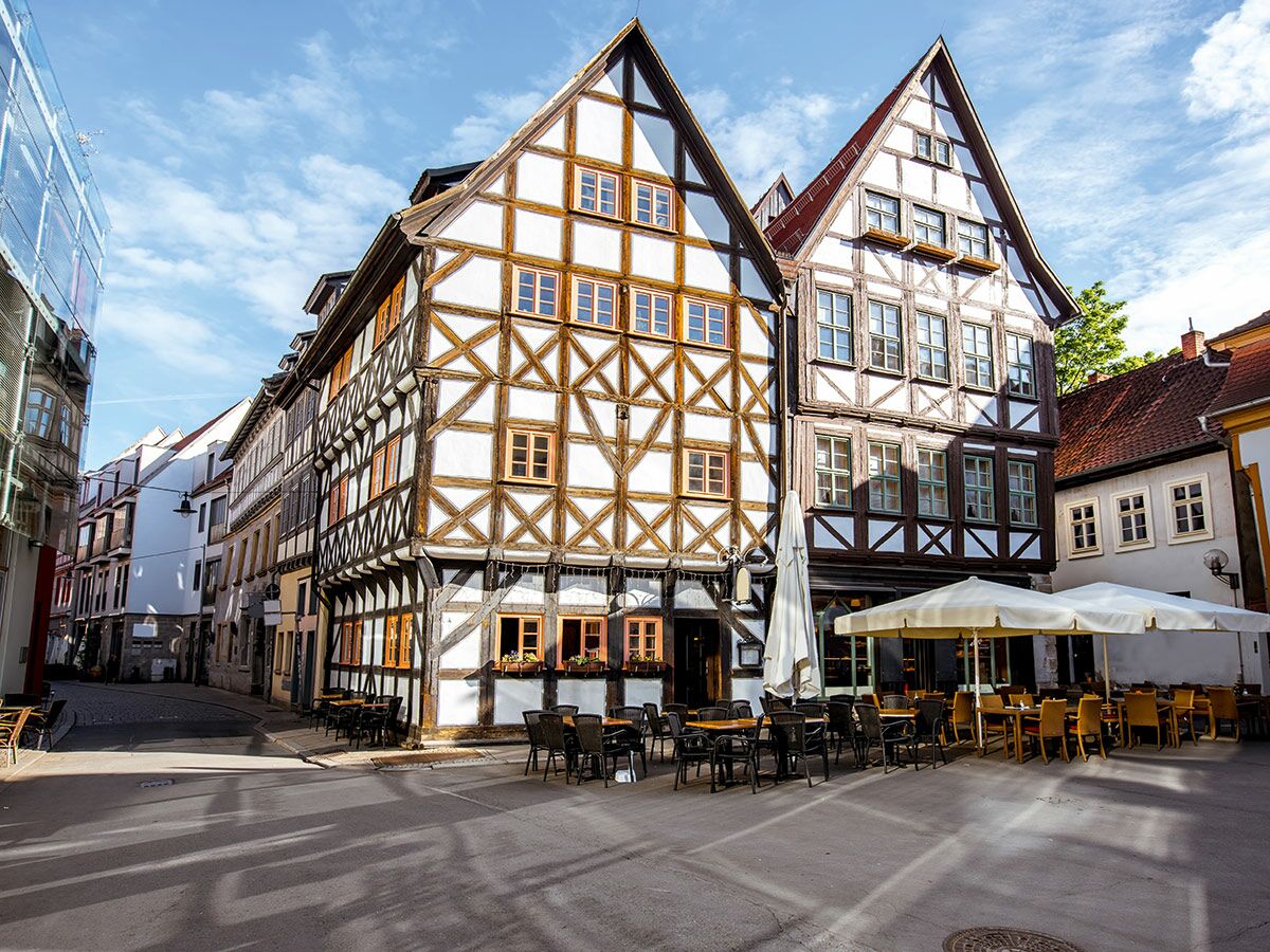 Fachwerkhäuser und Straßencafé bei Sonnenschein in europäischer Altstadt, gepflasterte Gasse.