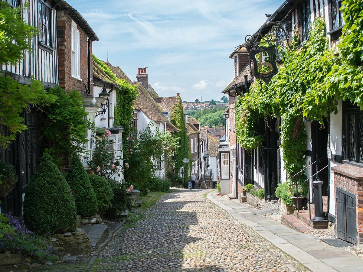 Die historische Mermaid Street in Rye, England, mit Kopfsteinpflaster, Fachwerkhäusern und üppigem Efeu unter blauem Himmel.