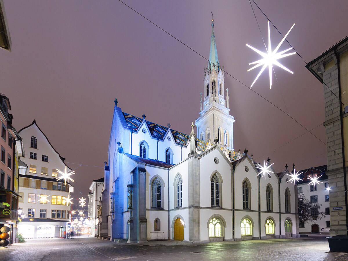 Die Peterskirche in Zürich bei Nacht, umgeben von historischen Gebäuden und beleuchtet mit festlichen Sternenlichtern.