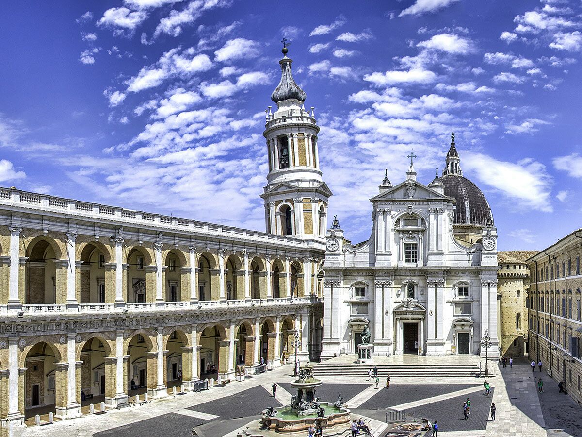 Luftaufnahme des Santuario della Santa Casa di Loreto mit Glockenturm, Säulengang, Platz und Springbrunnen unter blauem Himmel.