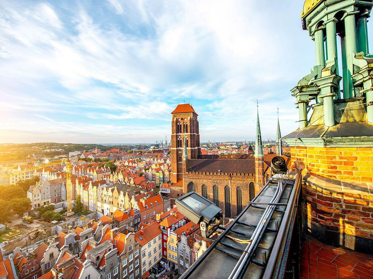 Historische Altstadt von Gdańsk bei Sonnenaufgang mit Marienkirche, roten Dächern und Stadtsilhouette vom Dach aus gesehen.