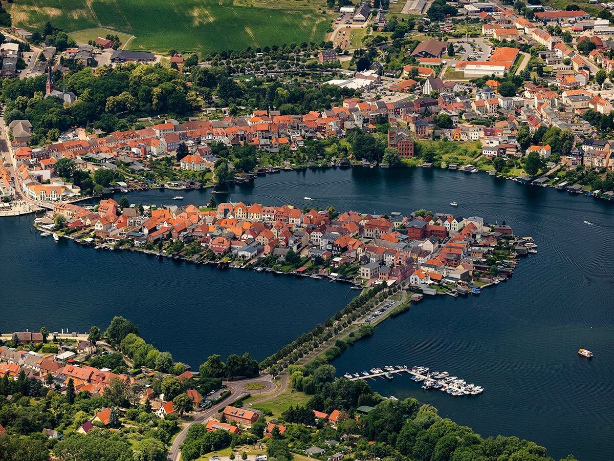 Luftaufnahme von Ratzeburgs Altstadtinsel mit rot gedeckten Häusern, umgeben vom Ratzeburger See und grüner Landschaft.