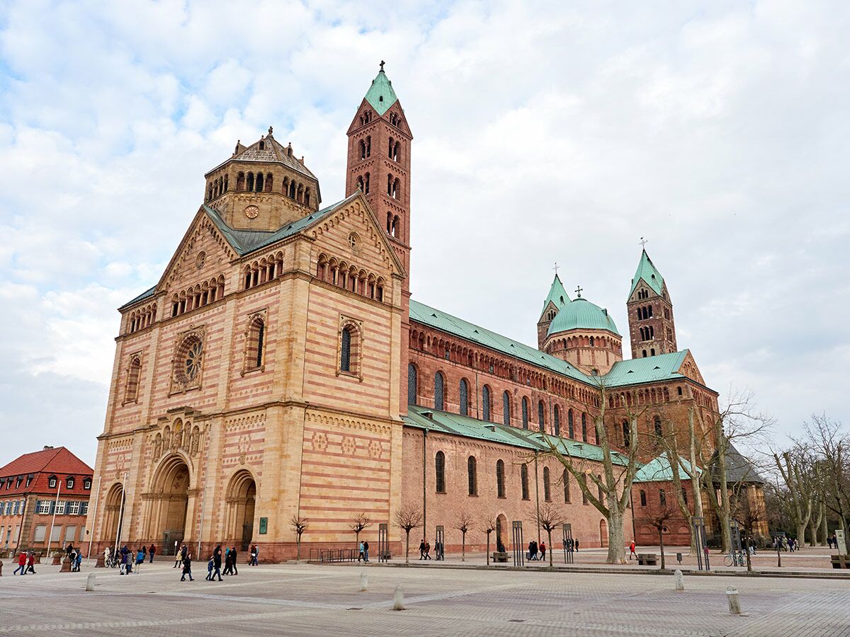 Gesamtansicht des Speyer Doms, einer romanischen Kathedrale mit gestreifter Fassade und grünen Kupferdächern, am Tag.
