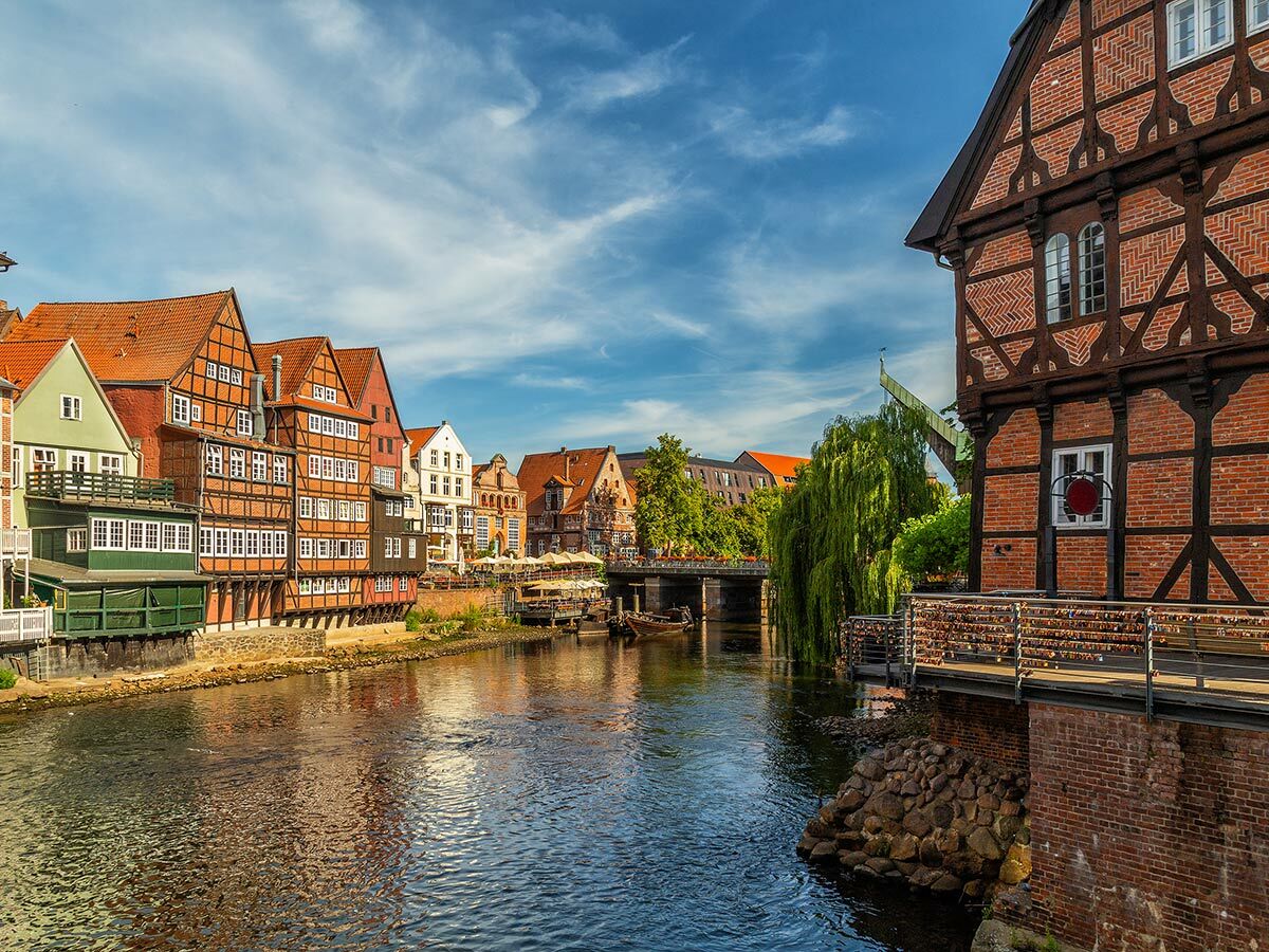 Malerische Fachwerkhäuser entlang eines Flusses in historischer deutscher Stadt Lüneburg unter blauem Himmel mit Brücke &amp; Liebesschlössern.