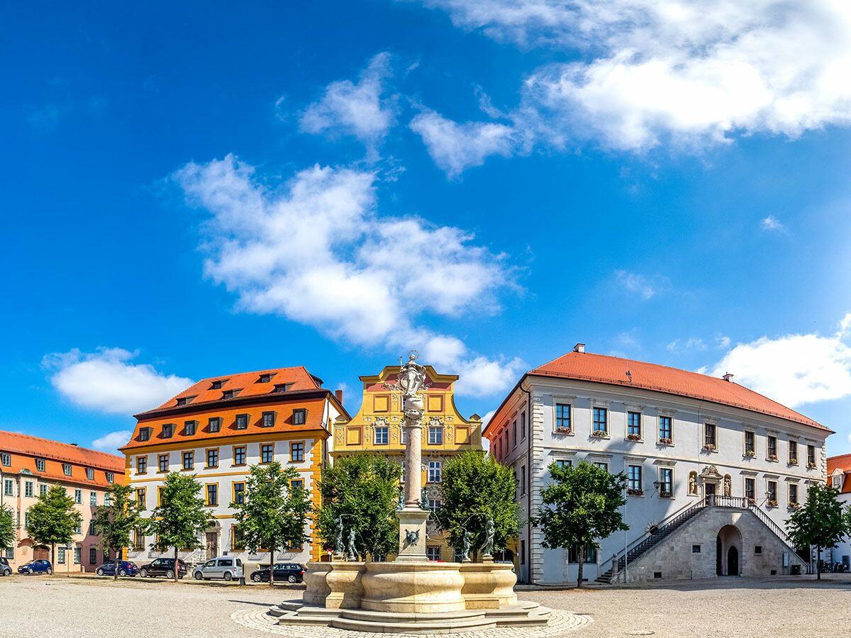 Historischer Gabelmann Brunnen auf dem Maxplatz in Bamberg, umgeben von barocken Gebäuden unter blauem Himmel.