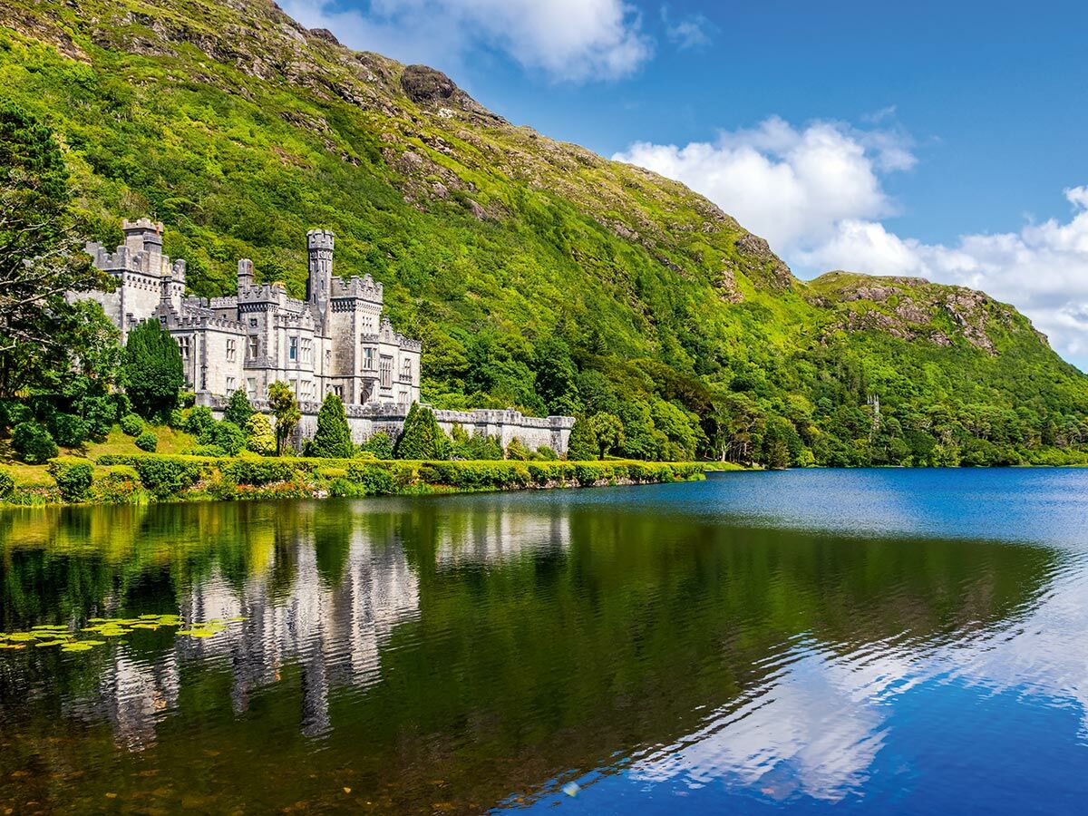 Majestätische Kylemore Abbey am Ufer des Pollacappall Sees, umgeben von grünen Bergen in Connemara, Irland, bei Sonnenschein.