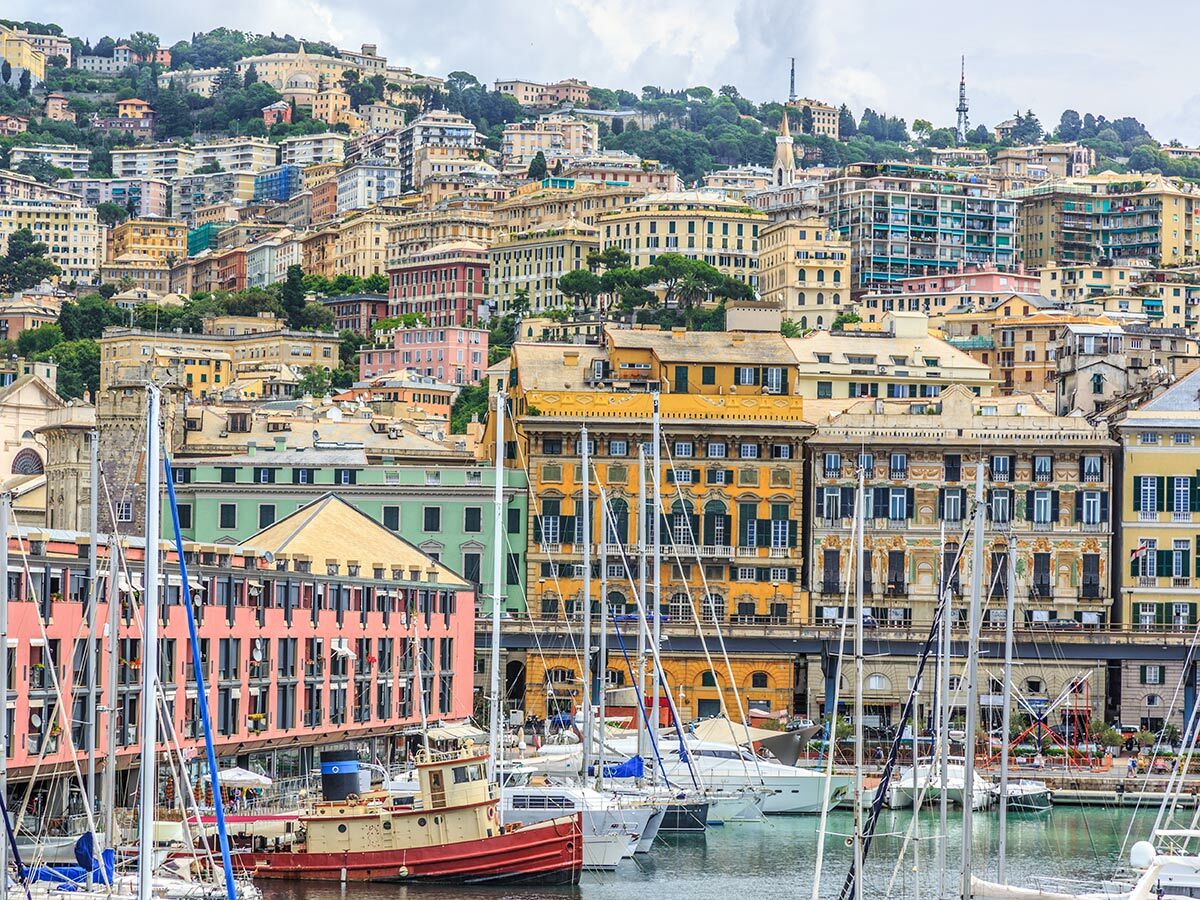 Panoramablick auf den Hafen von Genua mit vielen Segelbooten und bunten Häusern, die sich terrassenförmig an den Hügeln erstrecken.