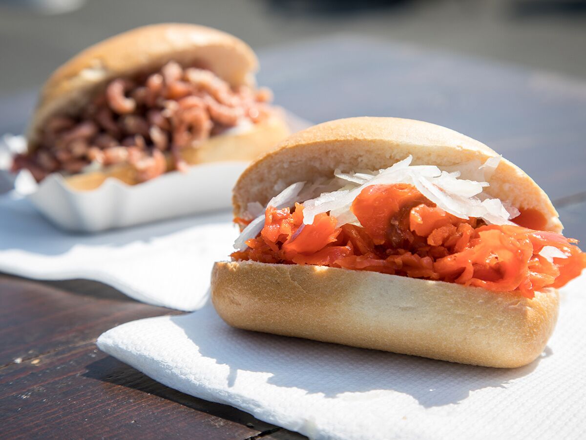 Zwei norddeutsche Fischbrötchen auf einem Holztisch: eines mit Krabben, das andere mit Lachs und Zwiebeln.