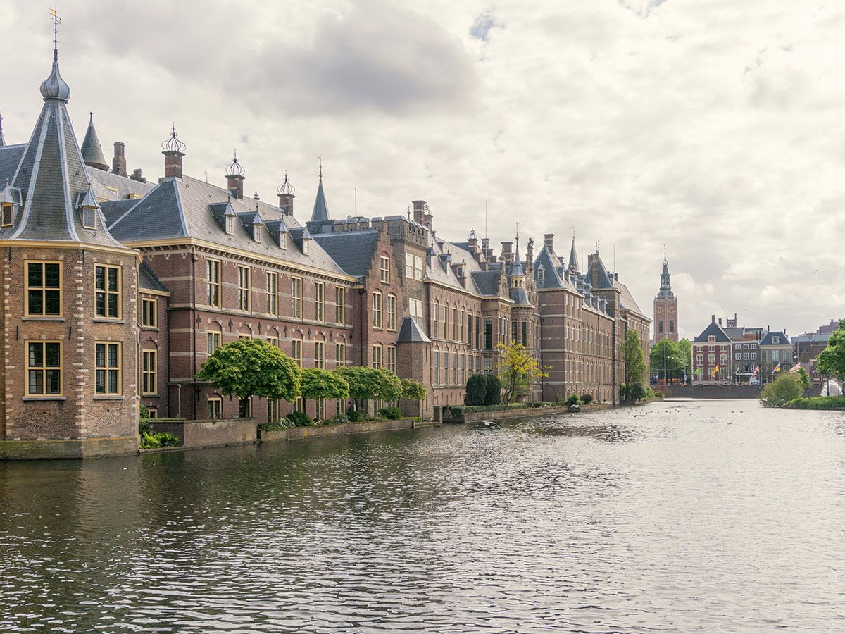 Historisches Binnenhof Regierungsgebäude in Den Haag, Niederlande, entlang einer Gracht unter bewölktem Himmel.