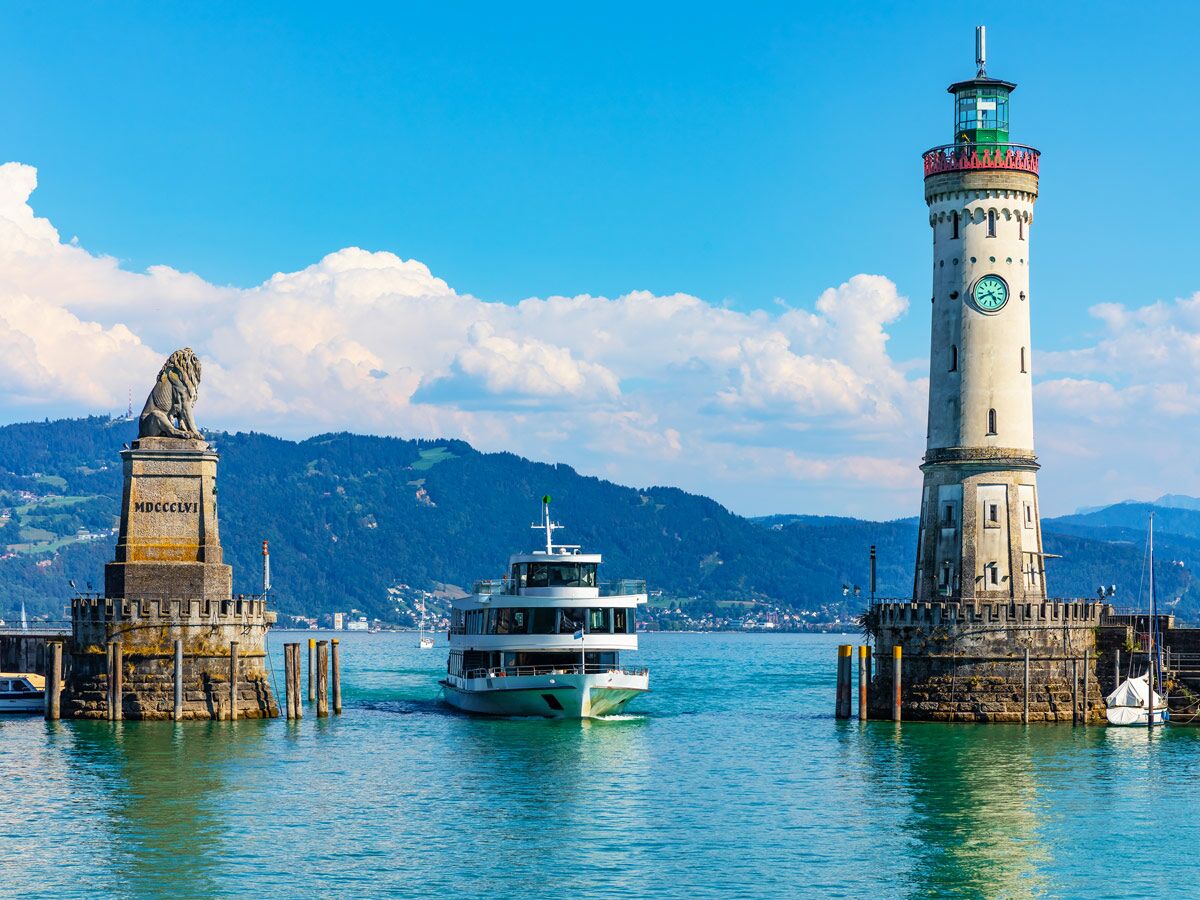 Lindau Hafen mit Leuchtturm, bayerischem Löwen und einem Schiff auf dem Bodensee bei Sonnenschein und blauem Himmel.