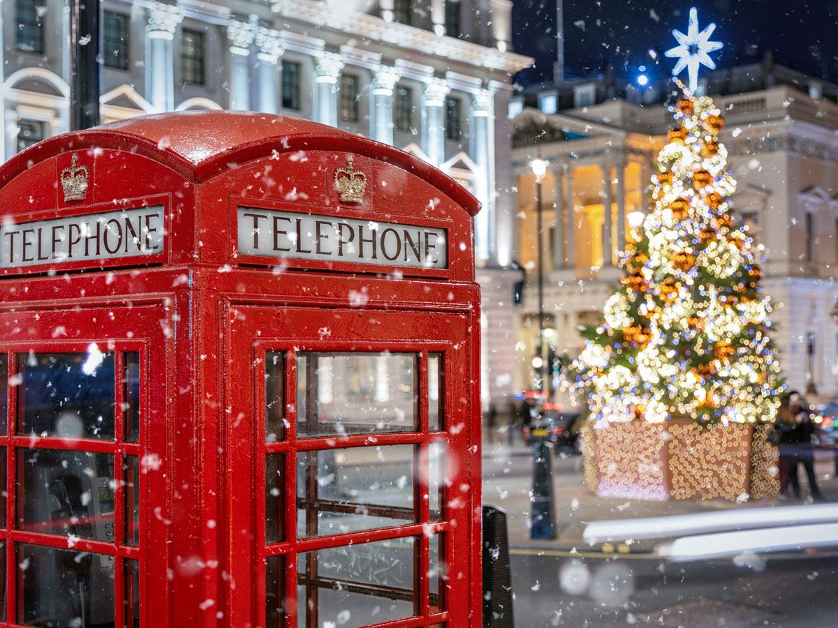 Rote Londoner Telefonzelle im Schnee mit beleuchtetem Weihnachtsbaum und historischen Gebäuden bei Nacht.