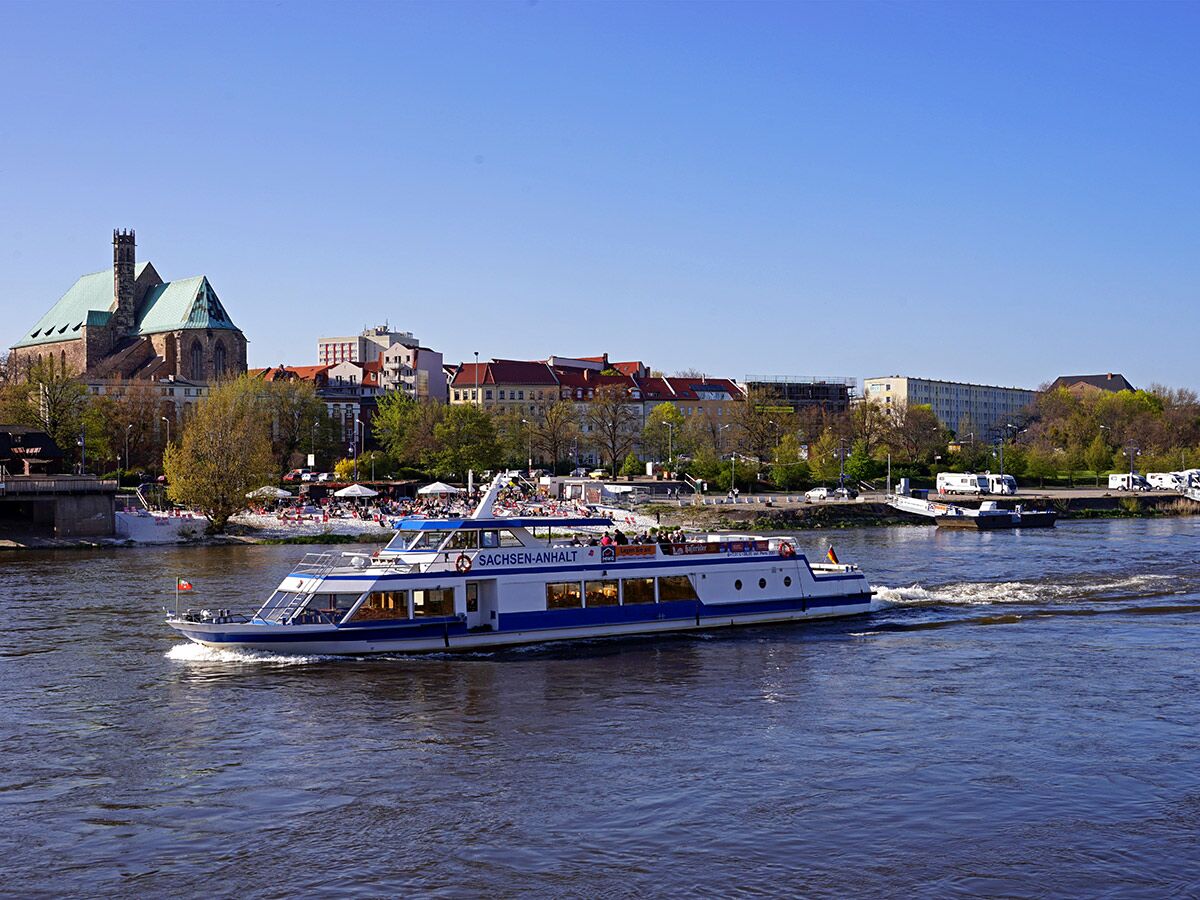 Passagierschiff SACHSEN-ANHALT auf der Elbe in Magdeburg, fährt vorbei an der Stadtkulisse mit Kathedrale und Menschen am Flussufer.