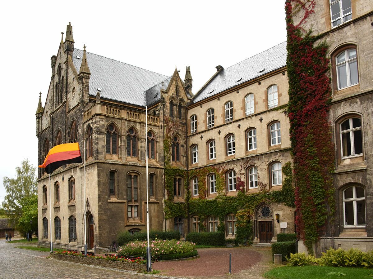 Historisches Universitätsgebäude in Deutschland, Steinfassade mit gotischen Elementen, rotem Herbst-Efeu und deutscher Flagge im Innenhof.