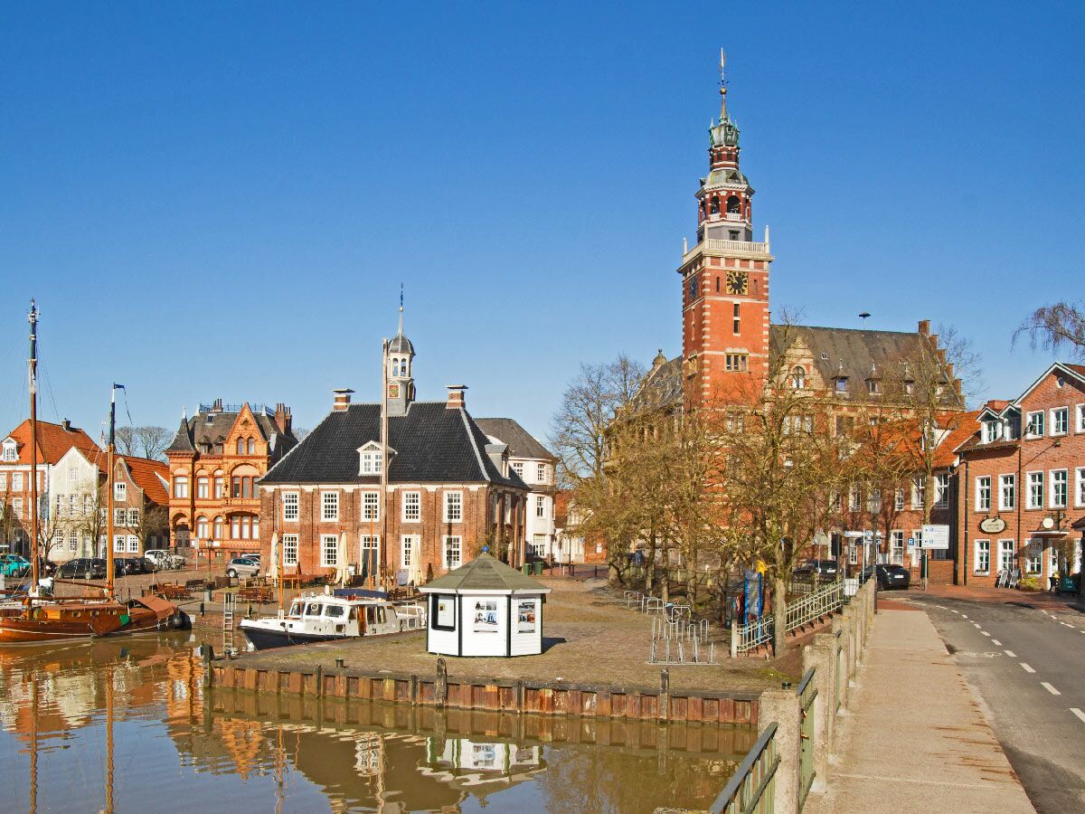 Blick auf die historische Hafenstadt Stade mit Altem Rathaus, Schwedenspeicher, Booten im Hansehafen und blauem Himmel.
