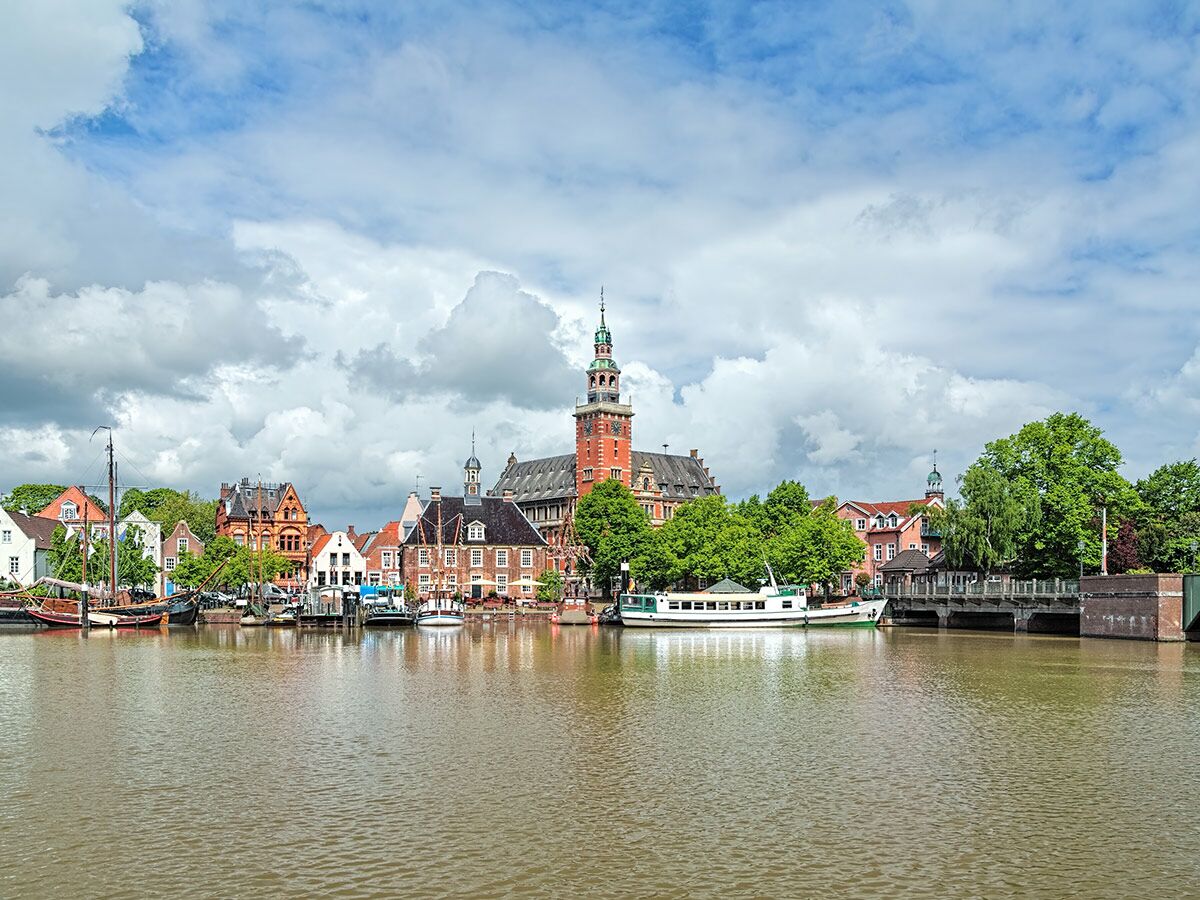 Historische Altstadt von Leer in Ostfriesland mit dem Rathaus am Hafen und Booten unter bewölktem Himmel.
