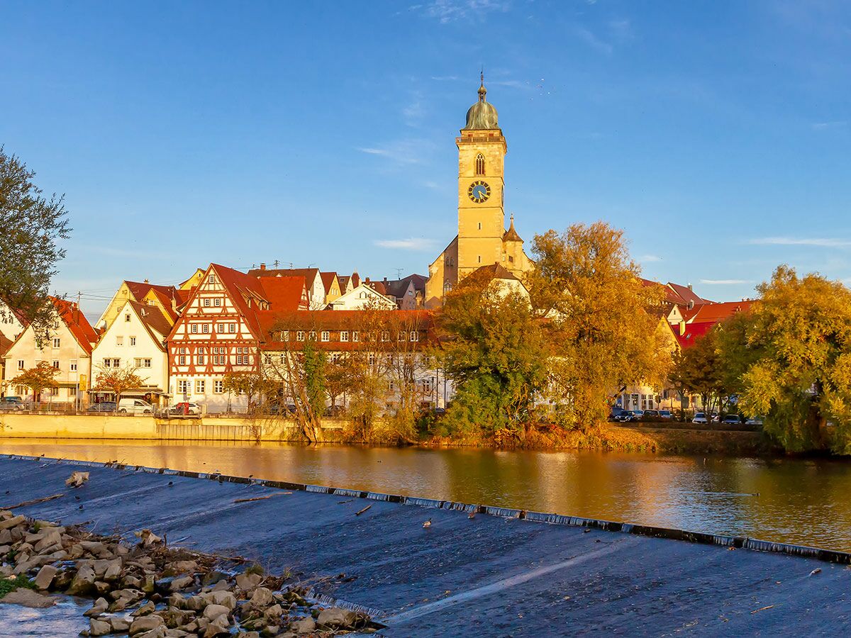 Historische Altstadt Tübingen am Neckar im Herbstlicht mit Stiftskirche, Fachwerkhäusern und Flusswehr bei Sonnenuntergang.
