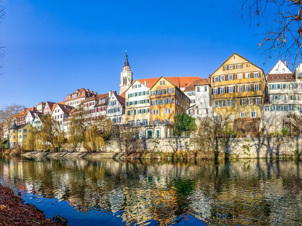 Bunte Häuser der Tübinger Neckarfront spiegeln sich idyllisch im Fluss Neckar unter strahlend blauem Himmel.