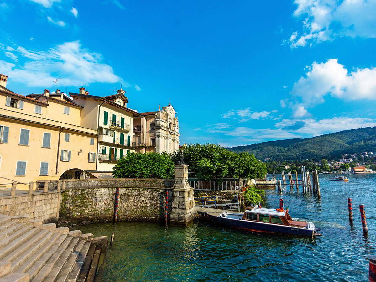Malerische italienische Stadt am Seeufer mit traditionellen Gebäuden, Kirche, Bergen und Booten unter blauem Himmel.
