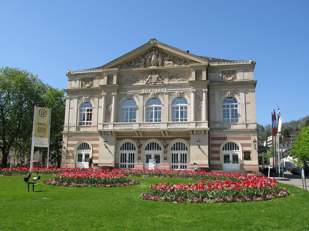 Historisches Theatergebäude in Baden-Baden mit Säulen, blühenden Tulpen und grünem Rasen an einem sonnigen Frühlingstag.