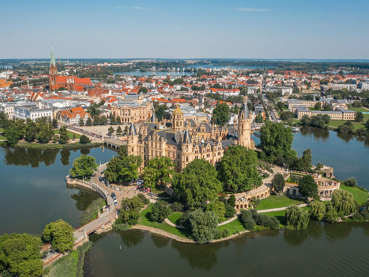Luftaufnahme des prachtvollen Schweriner Schlosses auf einer Insel im See mit der Stadt Schwerin und blauem Himmel.
