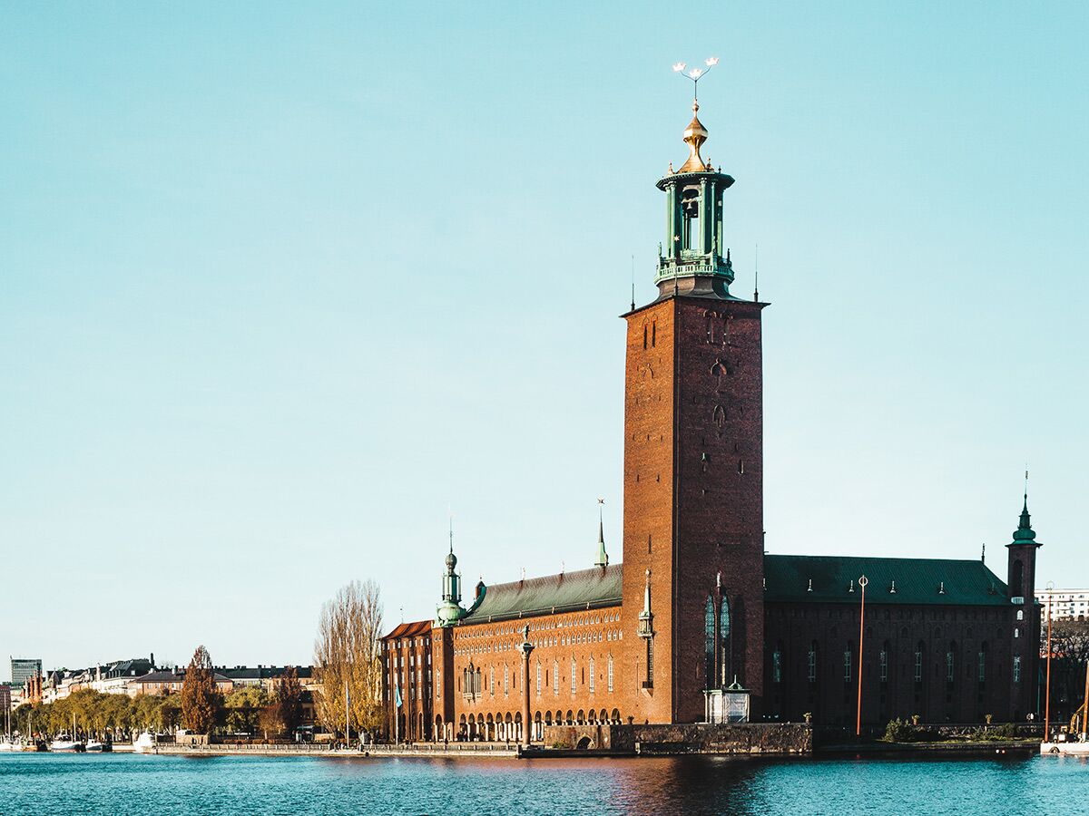 Panoramablick auf das historische Stockholmer Rathaus aus rotem Backstein mit markantem Turm und goldenem Dach am Wasser.