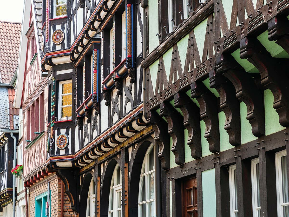Detaillierte Ansicht traditioneller Fachwerkhäuser mit bunten Holzbalken, verzierten Fenstern und historischen Verzierungen in einer Altstadtgasse.