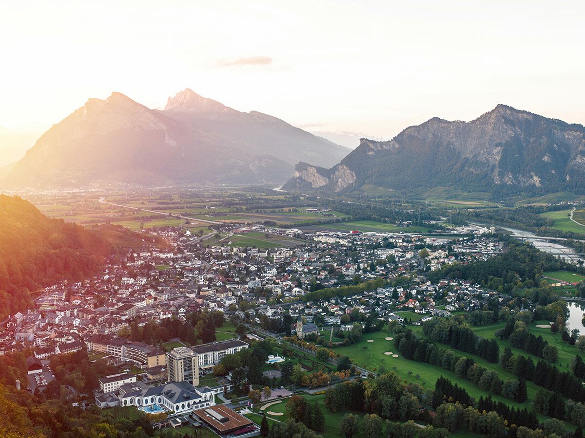 Panoramablick auf Vaduz, Liechtenstein, mit der Stadt, dem Rhein, den umliegenden Alpen und einem Golfplatz.