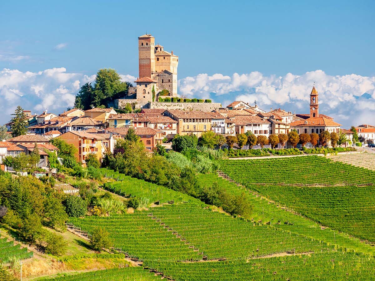 Historisches Dorf Serralunga d'Alba im Piemont mit Burg, Kirche und Weinbergen unter blauem Himmel und Wolken.