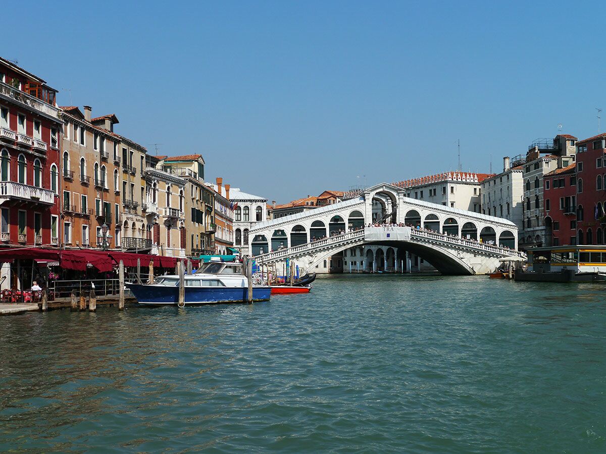 Panoramablick auf die Rialtobrücke in Venedig mit historischen Gebäuden und Booten auf dem Grand Canal unter blauem Himmel.