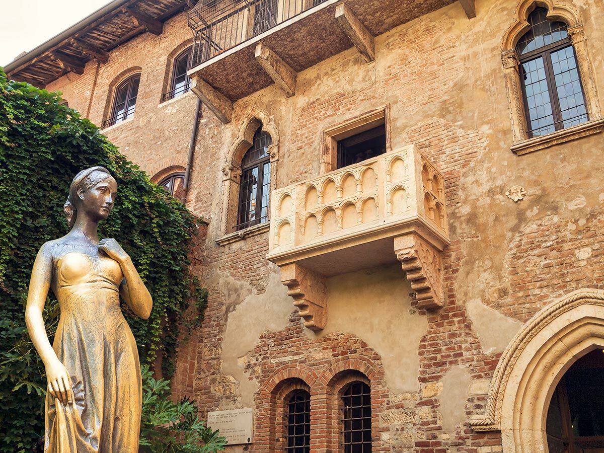 Bronzestatue von Julia vor dem historischen Haus mit dem berühmten Balkon in Verona, Italien, umrankt von Efeu.