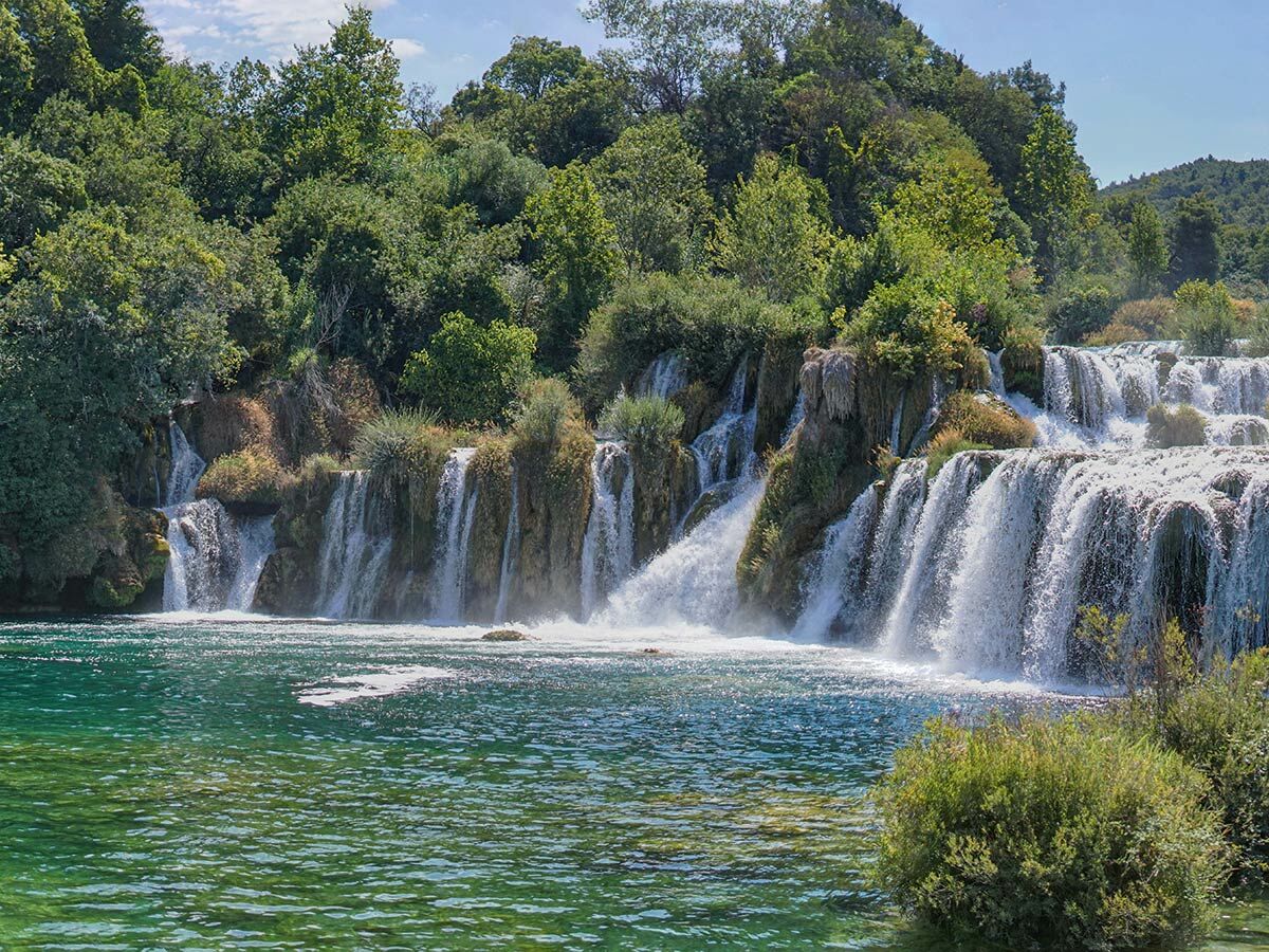 Mehrere Wasserfälle stürzen in türkisgrünes Wasser, umgeben von dichten Wäldern im Krka Nationalpark, Kroatien.