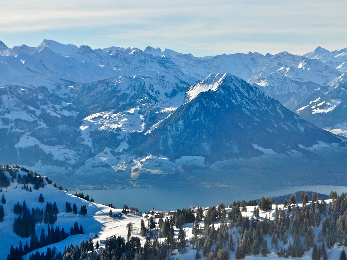 Majestätische Winterlandschaft der Alpen mit schneebedeckten Gipfeln, Tannenbäumen und einem ruhigen blauen See unter klarem Himmel.