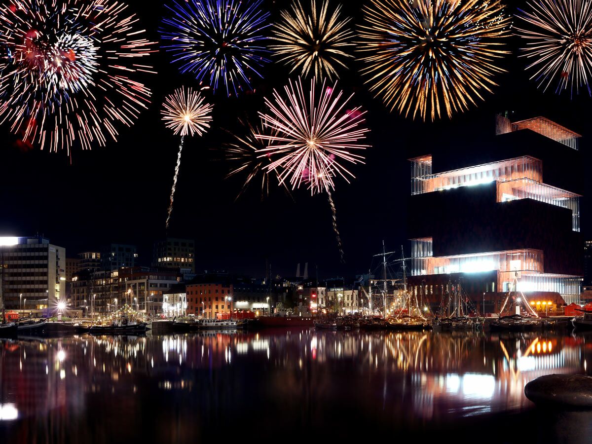 Farbenfrohes Feuerwerk erleuchtet den Nachthimmel über dem Hafen von Oslo mit dem Munch Museum und reflektierenden Lichtern im Wasser.