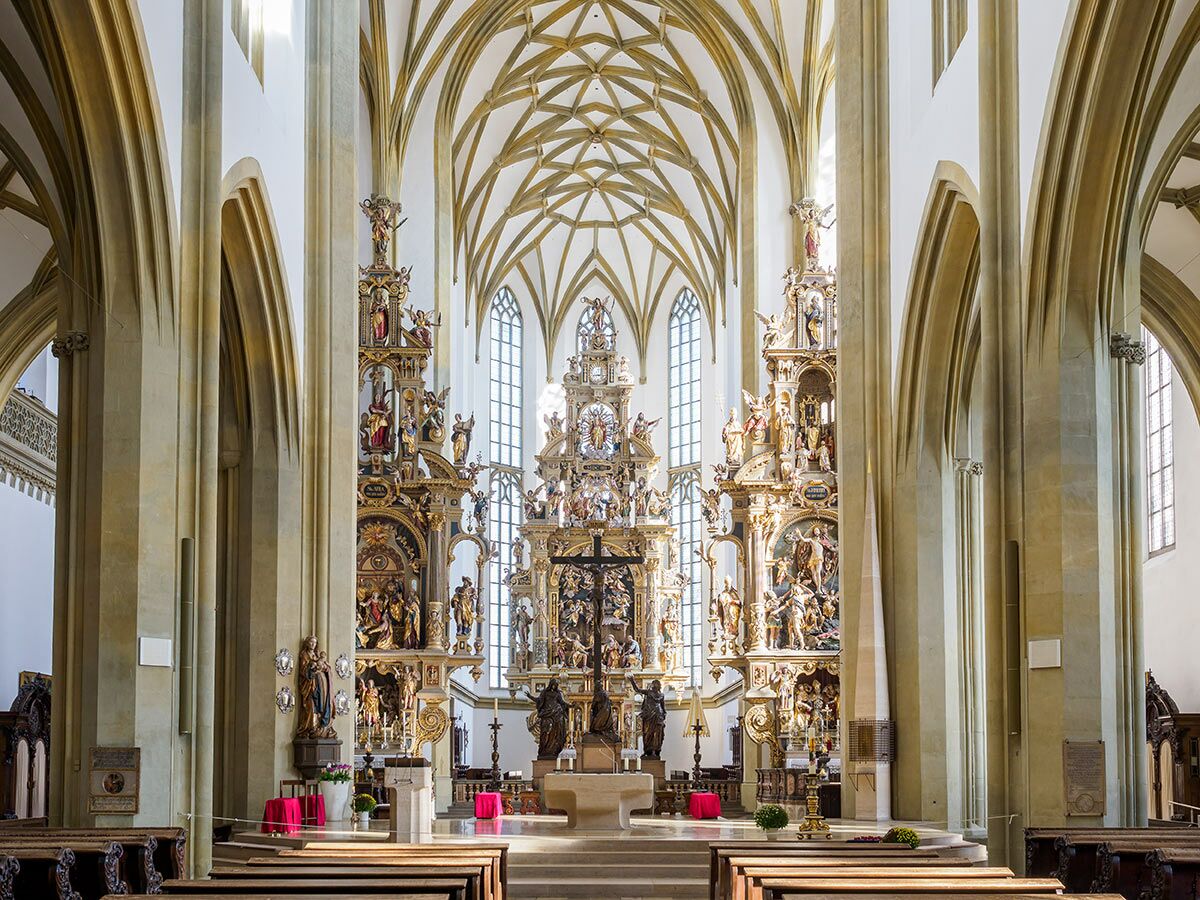 Innenansicht einer prächtigen Barockkirche mit detailreichem Hochaltar, hohen Säulen, Gewölbedecke und Kirchenbänken.