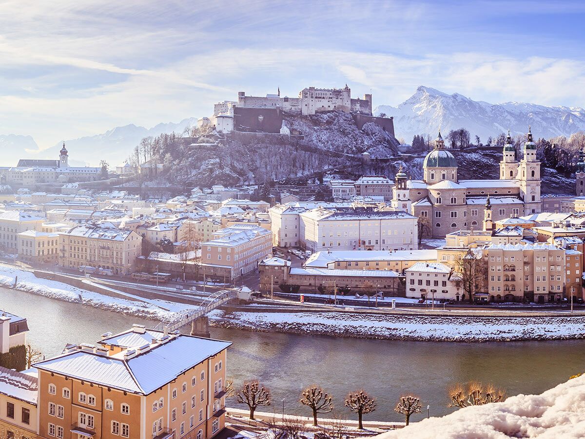 Winterliche Panoramasicht auf Salzburg mit der Festung Hohensalzburg, Salzach Fluss, Dom und verschneiten Bergen.