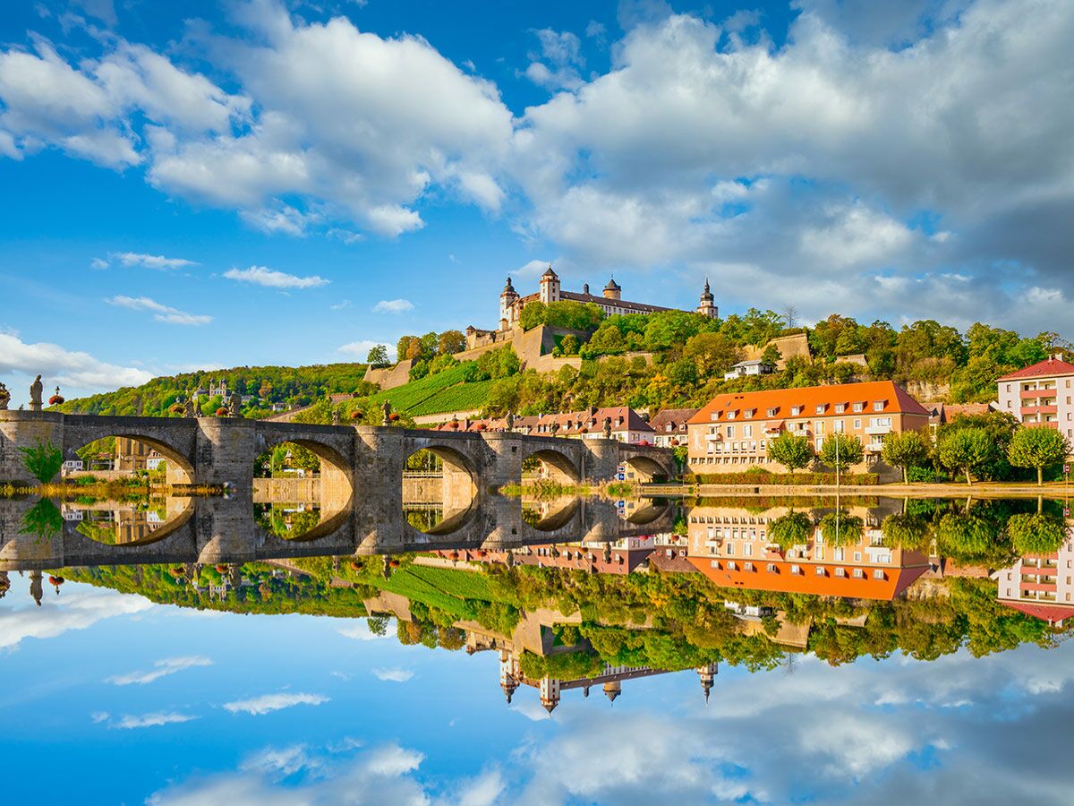 Historische Alte Mainbrücke in Würzburg mit Statuen und Festung Marienberg am Fluss Main unter blauem Himmel mit Wolken.