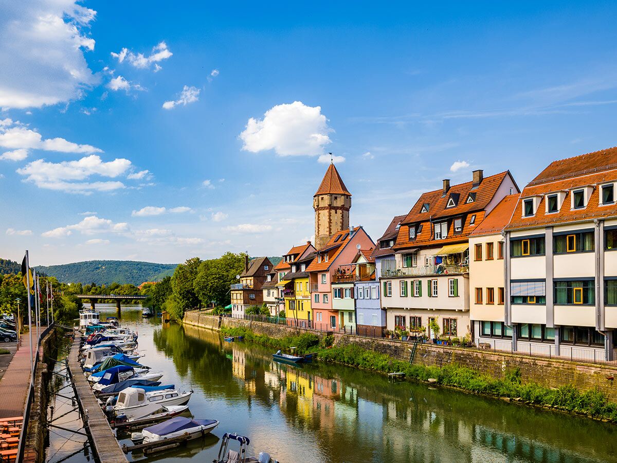 Bunte Gebäude, ein alter Turm und Boote entlang eines Flusses in einer malerischen deutschen Stadt bei Sonnenschein.