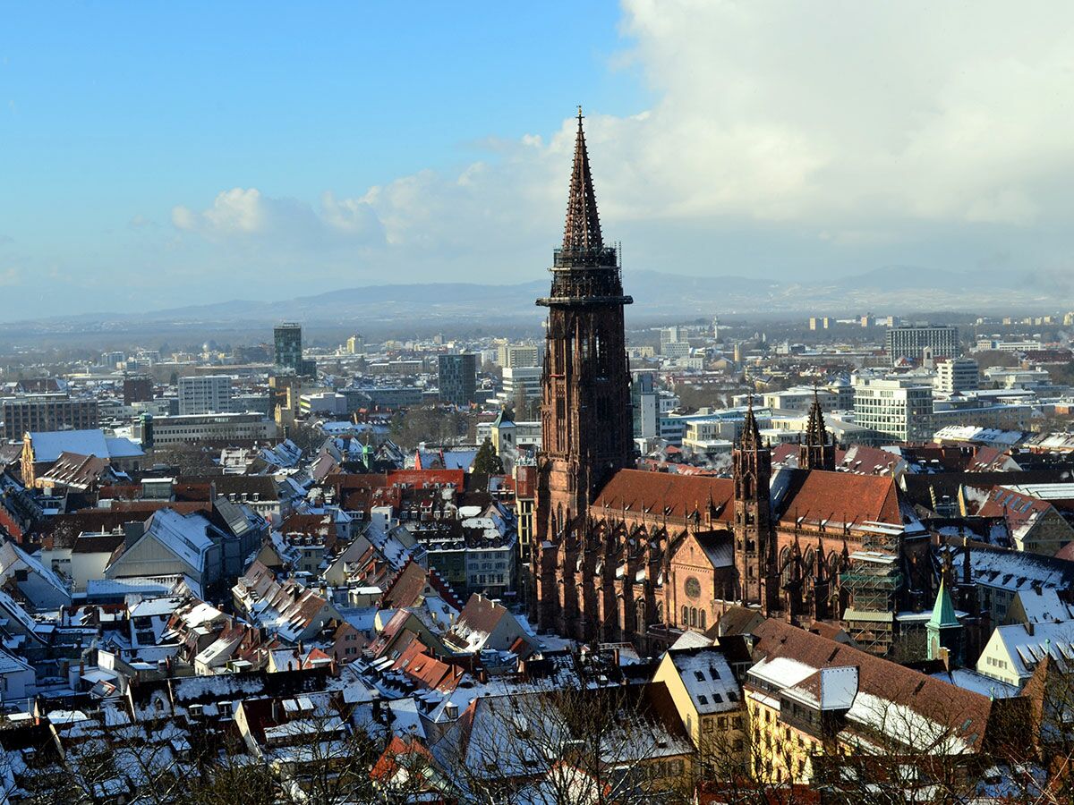 Verschneite Stadtansicht von Freiburg im Breisgau mit dem Freiburger Münster und Bergen im Winter.