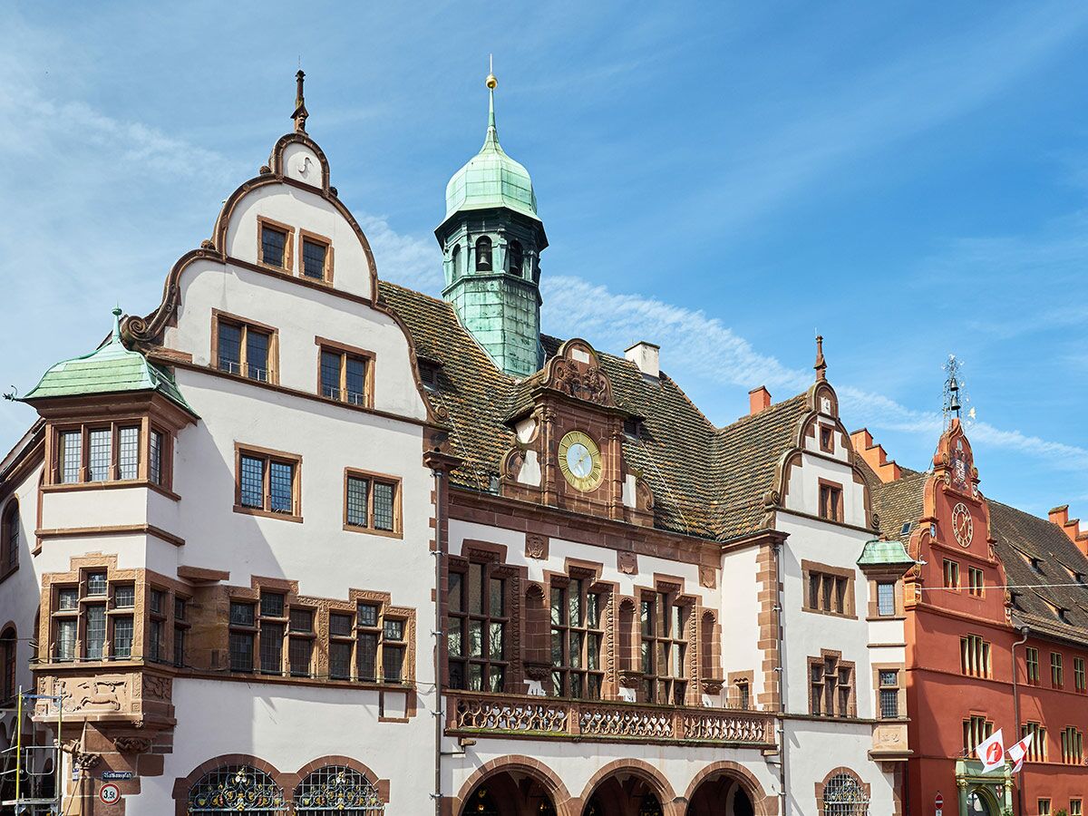 Historisches Rathaus in Freiburg im Breisgau mit Giebeln, Uhren, grünem Turm und bunter Fassade unter blauem Himmel.