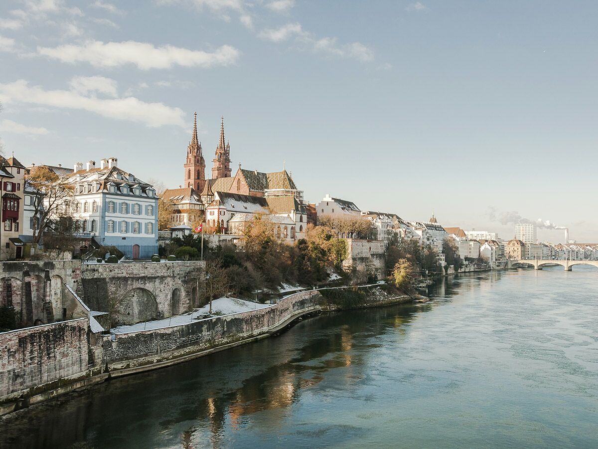 Winterliche Stadtansicht von Basel mit dem Münster am Rheinufer und historischen Gebäuden, etwas Schnee auf Dächern.