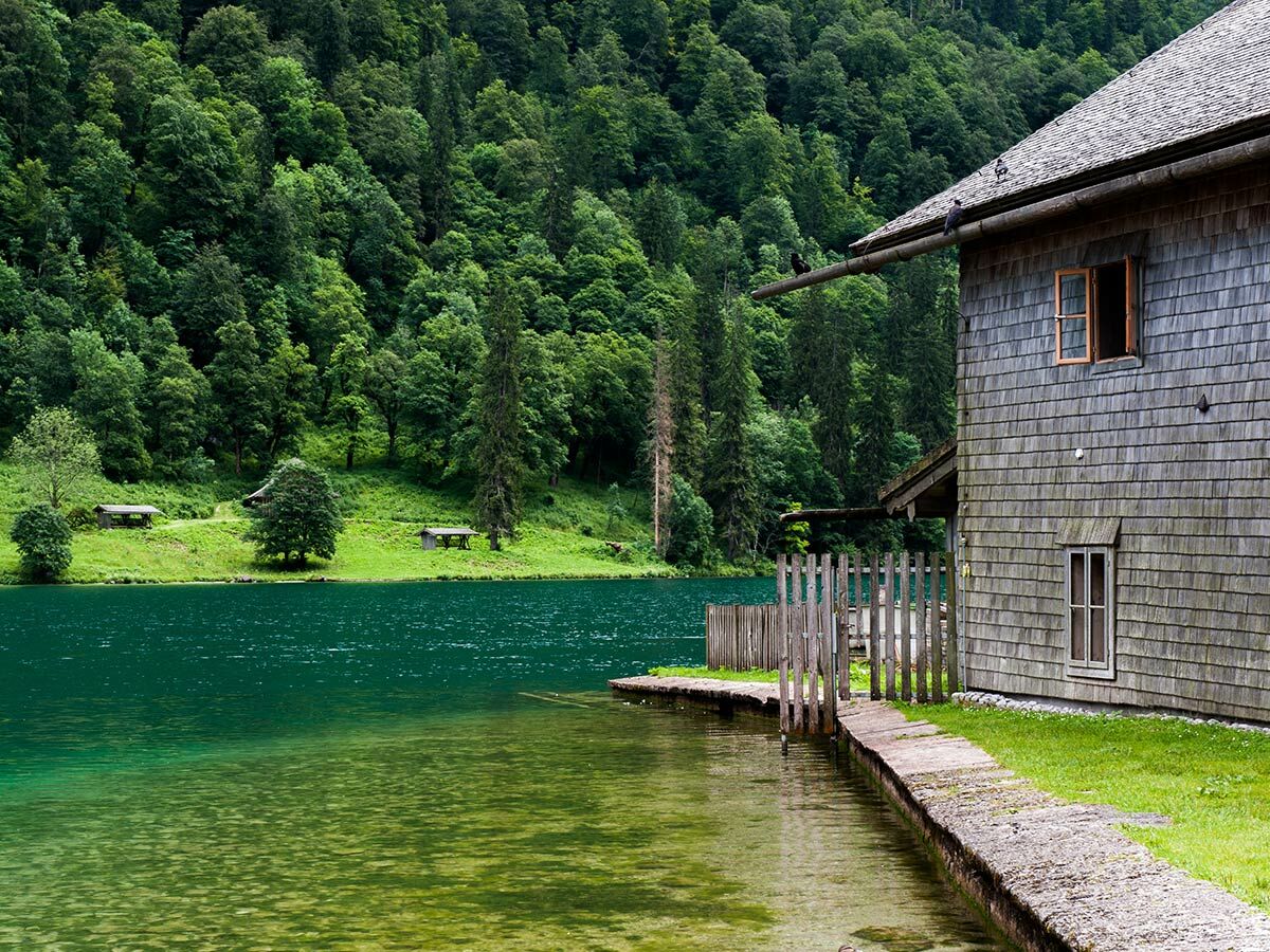 Idyllischer Bergsee mit klarem, türkisfarbenem Wasser und dichter Waldkulisse. Eine traditionelle Holzhütte steht direkt am Ufer.
