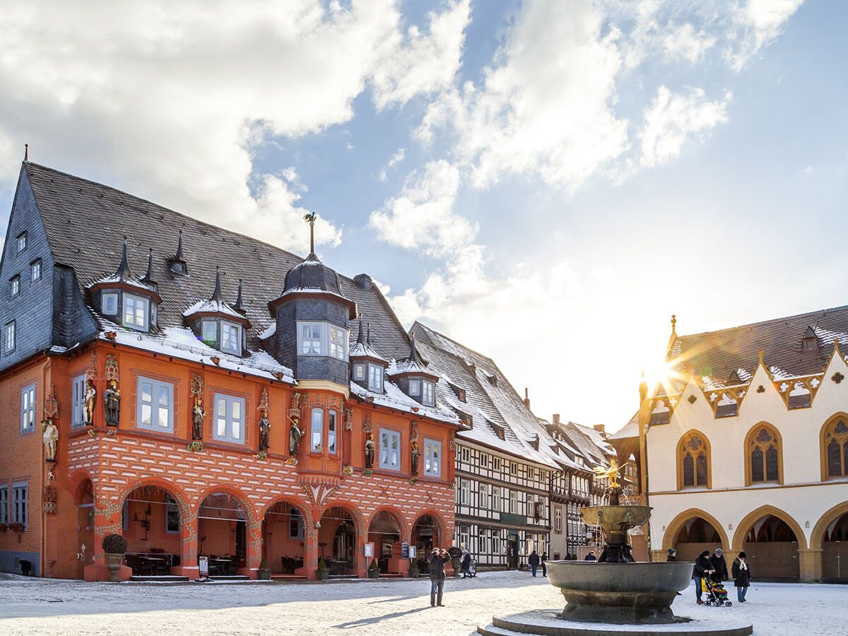 Historischer Marktplatz Goslar im Winter mit verschneiten Fachwerkhäusern, Brunnen und sonnigem Himmel.