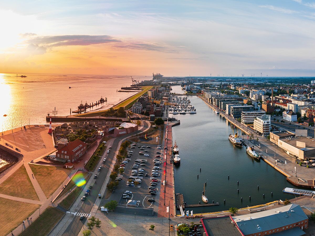 Luftaufnahme der Hafenstadt Bremerhaven bei Sonnenuntergang. Goldenes Licht über Meer, Leuchtturm, Yachthafen, Gebäude, Windräder.