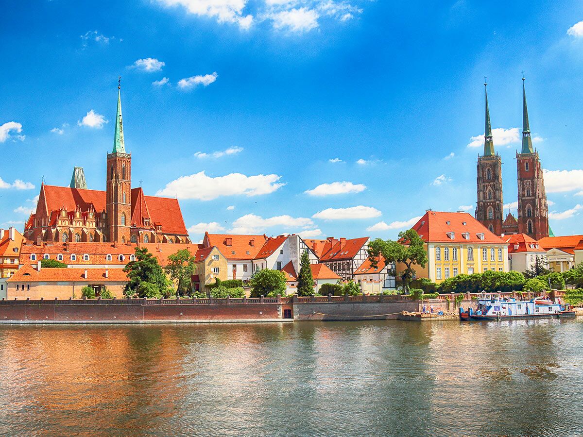 Wrocław Dominsel Panorama mit Kathedrale, historischen Gebäuden und Oder Fluss unter blauem Himmel. Boote am Ufer.