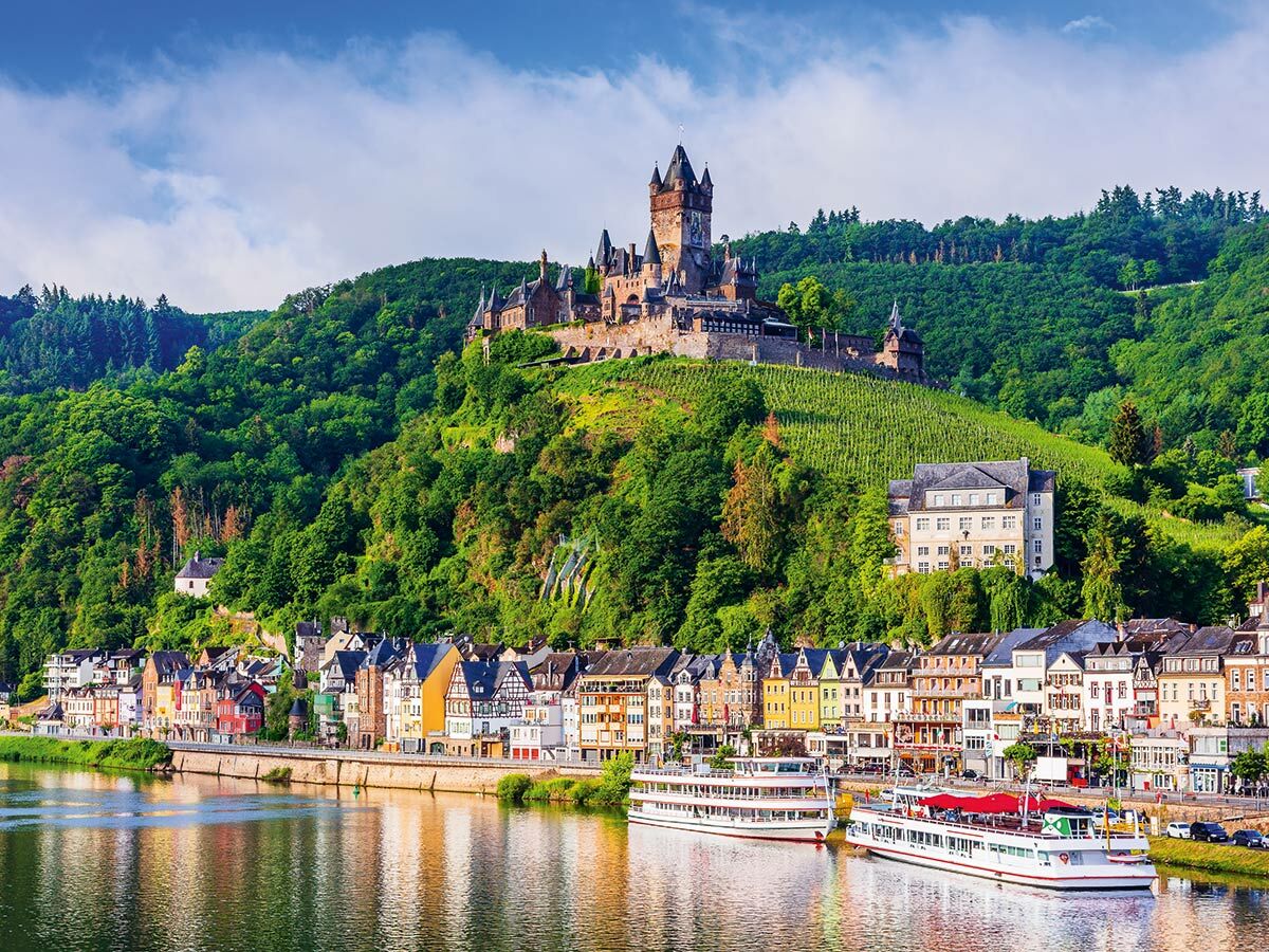 Panoramablick auf die Reichsburg Cochem, die Mosel, die bunten Häuser der Stadt und die umliegenden Weinberge.