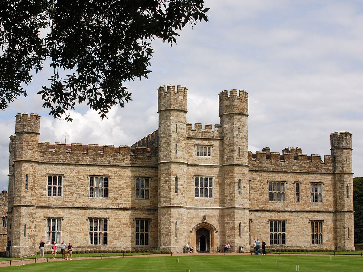 Blick auf Leeds Castle aus hellem Stein mit Türmen, vielen Fenstern und grüner Rasenfläche, umgeben von Touristen.