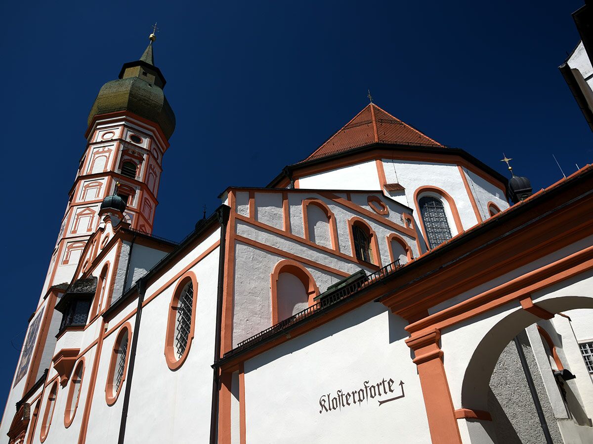 Historische Barockkirche oder Kloster mit Zwiebelturm, orangefarbenen Akzenten und blauem Himmel.