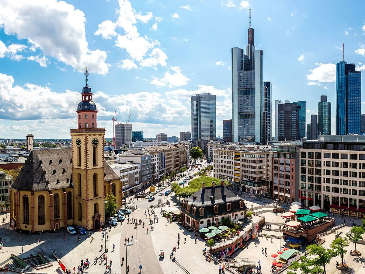 Panorama von Frankfurt am Main: Paulskirche, belebter Platz, moderne Wolkenkratzer und strahlend blauer Himmel mit Wolken.