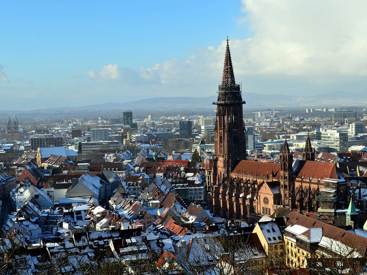 Panoramablick auf das Freiburger Münster und die verschneite Altstadt im Winter unter blauem Himmel.